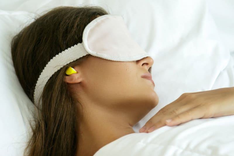 A woman sleeping with earplugs and a mask.